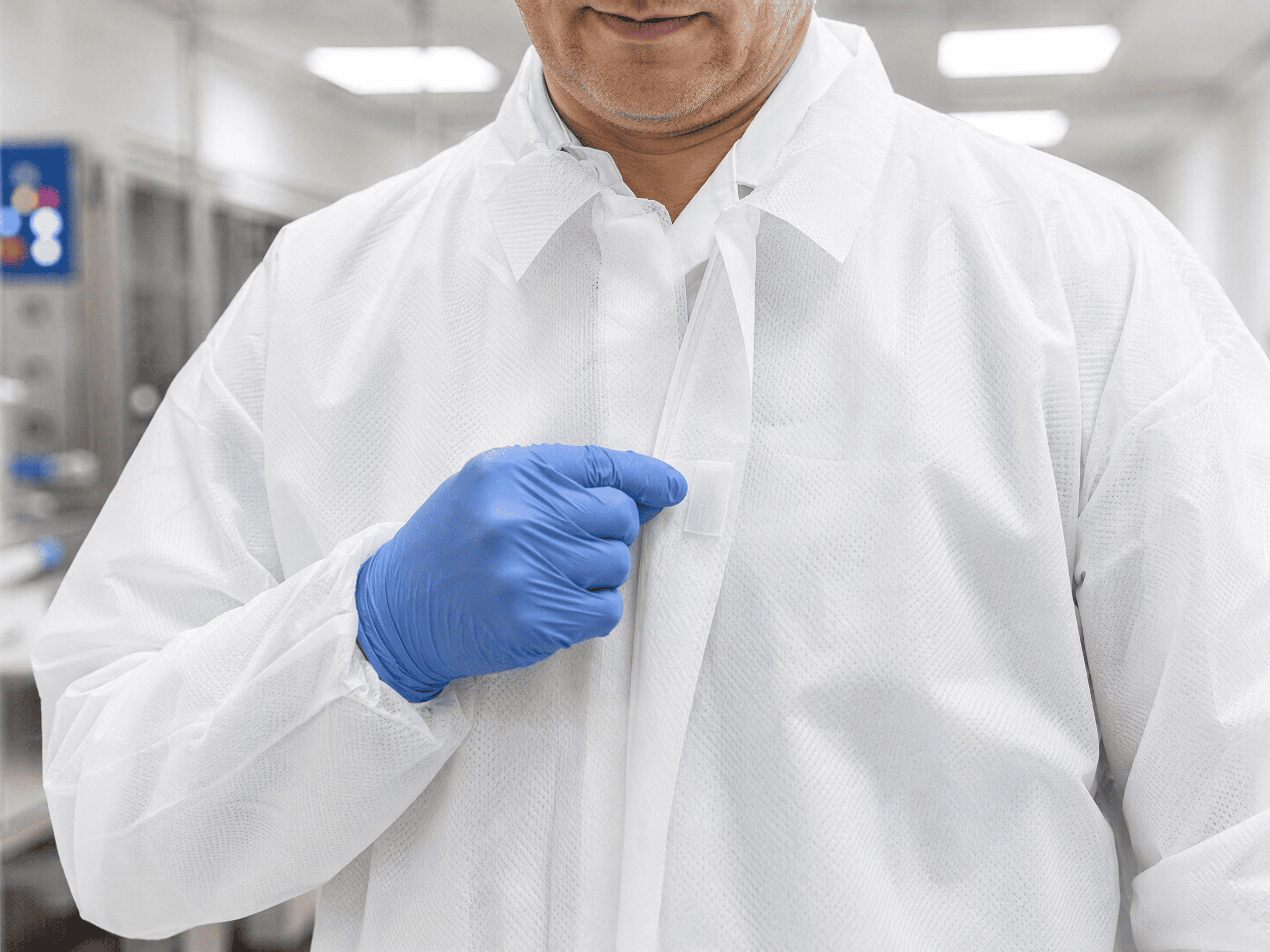 Blouse jetable blanche &agrave; fermeture velcro port&eacute;e par un op&eacute;rateur qui l'ajuste d'un geste avec un gant